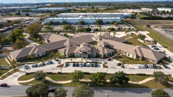 Aerial view of a large building complex with a parking lot and green spaces in a suburban setting.