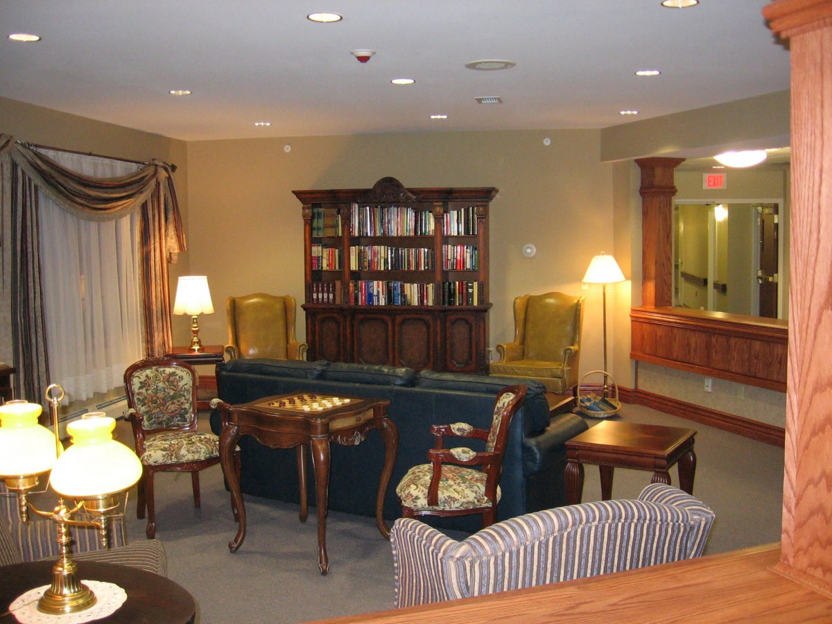 A cozy indoor reading area with a bookshelf, chairs, and lamps.