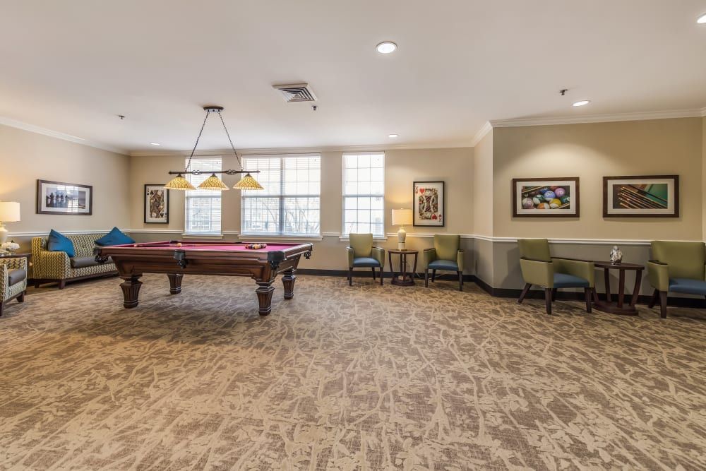 A spacious billiards room with a pool table, seating, and artwork on the walls.