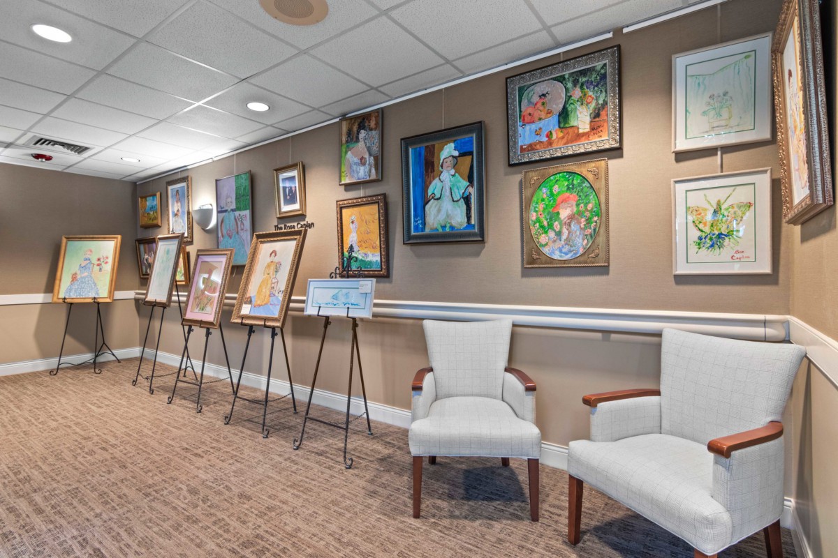 An art gallery with paintings displayed on the walls and easels, accompanied by comfortable seating.