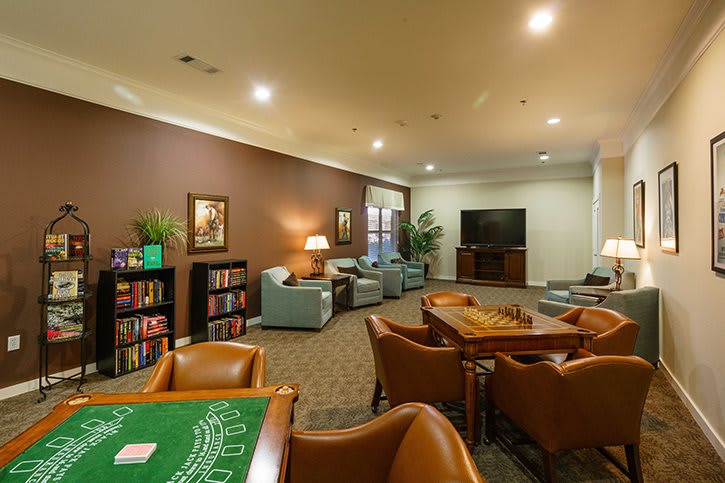 A cozy lounge area featuring armchairs, wooden tables, a television, and bookshelves.