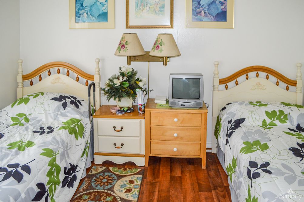 A cozy bedroom with twin beds and floral bedding, featuring a shared nightstand with a lamp and a small television.