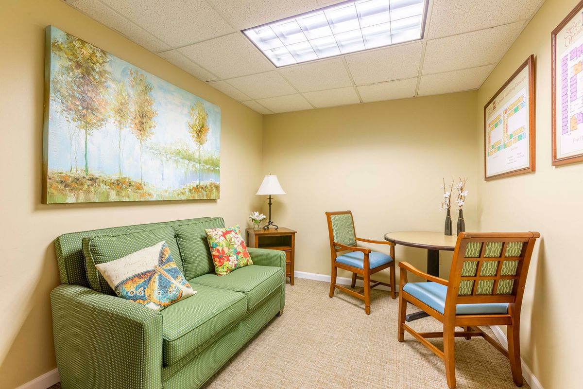 A cozy office waiting room with a green sofa, two chairs, a small table, and artwork on the wall.