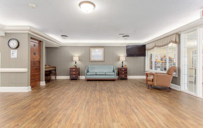 A spacious living room with wooden flooring, featuring a couch, lamps, and a television.