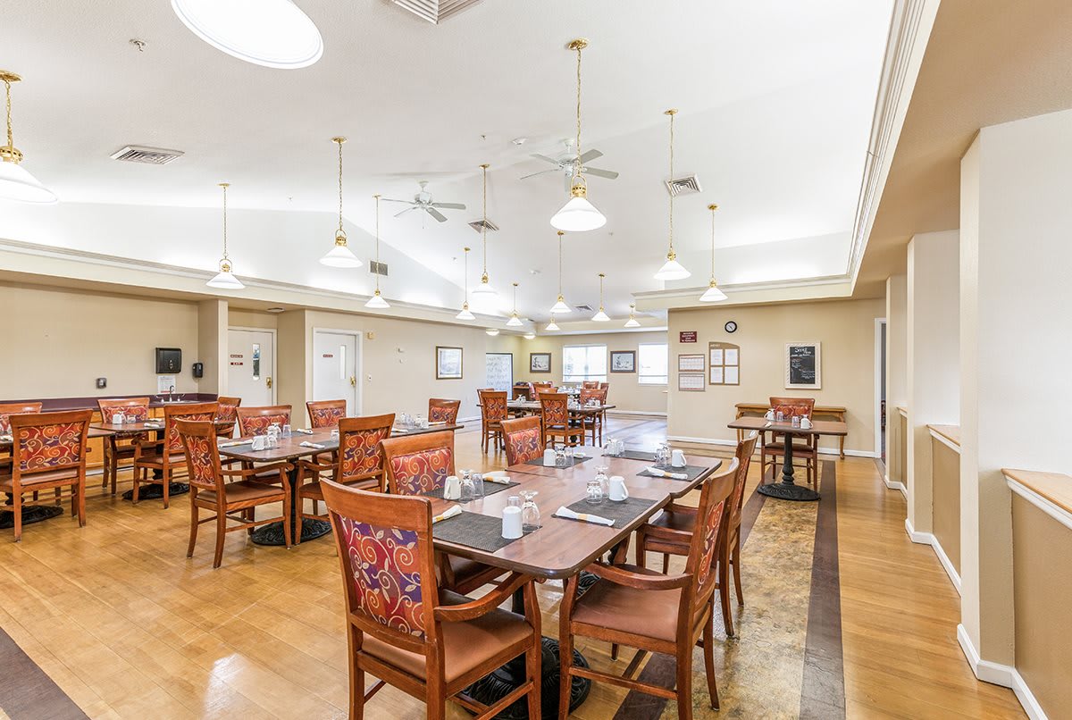 A spacious dining room with elegant tables and chairs, featuring ceiling lights and a wooden floor.