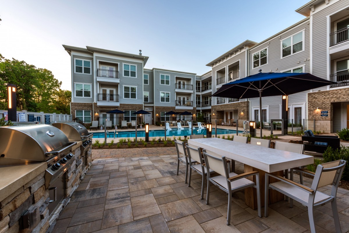 A modern apartment complex featuring a pool and outdoor seating area at sunset.