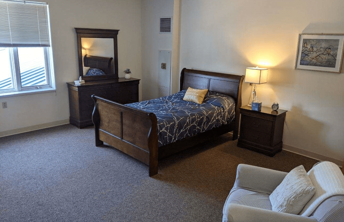 A cozy bedroom featuring a wooden bed, matching dresser with mirror, and a bedside lamp.