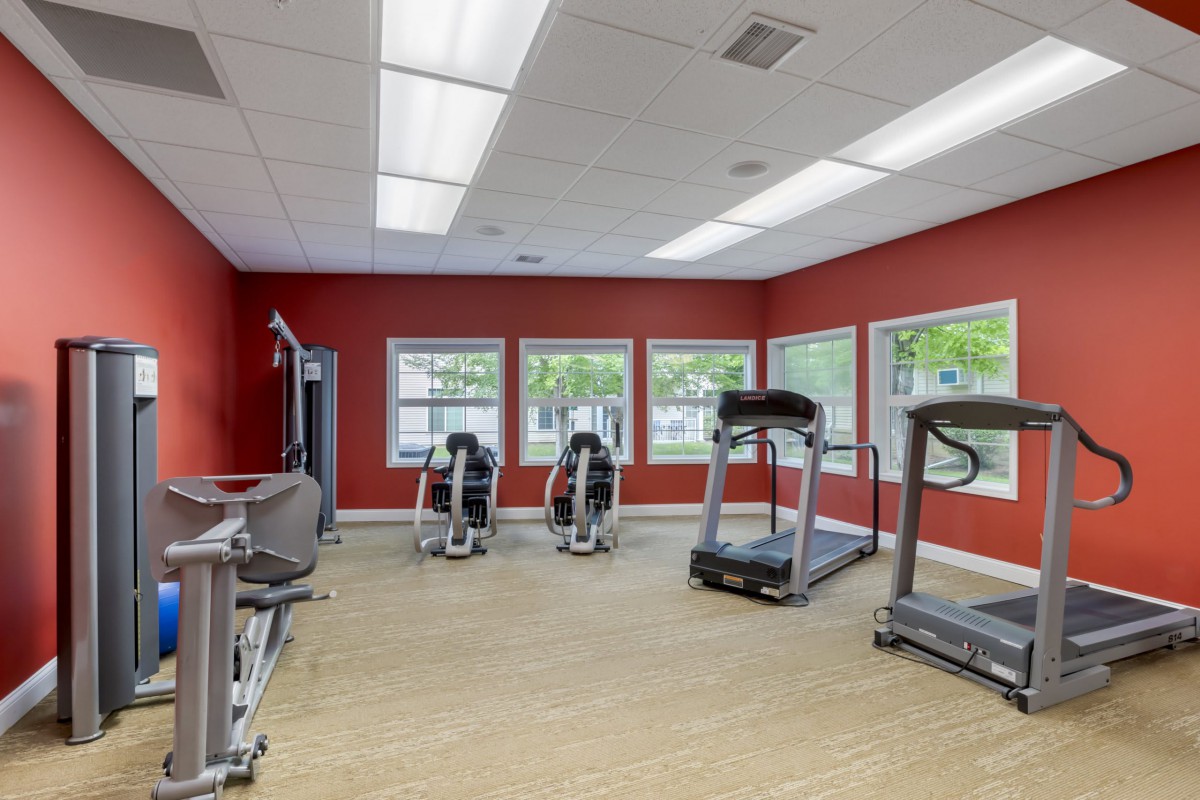 A well-lit gym with treadmills and stationary bikes next to large windows.