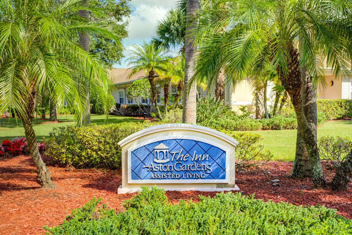 A landscaped area with a decorative sign in front of a building, surrounded by palm trees and gardens.