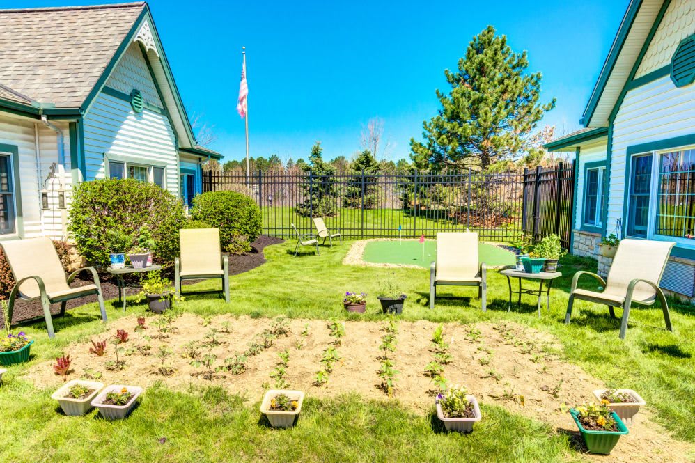 A sunny backyard with lawn chairs and a small garden plot.