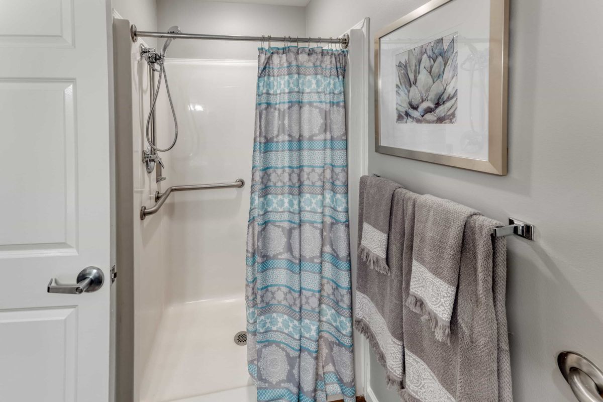 A well-organized bathroom with a shower area, featuring a patterned shower curtain, neatly hung towels on a rack, and framed artwork on the wall.