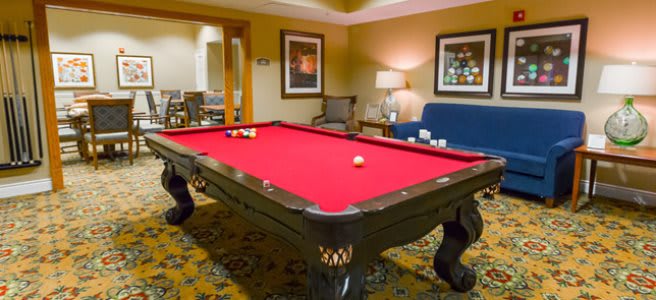 A cozy game room featuring a red-felt pool table surrounded by comfortable seating.