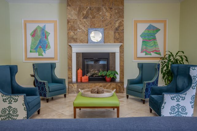 A cozy modern living room with a fireplace, surrounded by elegant blue armchairs and vibrant artwork.