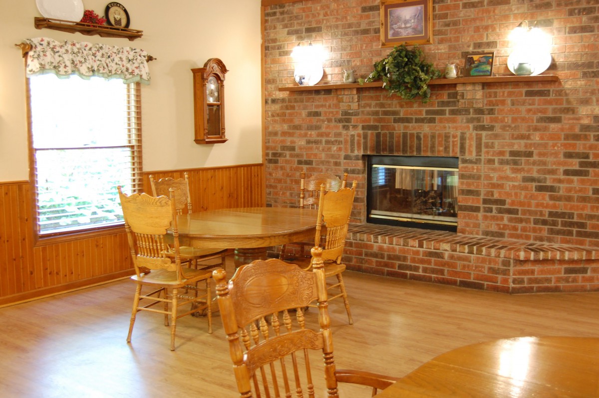 A cozy dining room featuring a round wooden table and chairs, with a brick fireplace and hardwood flooring.