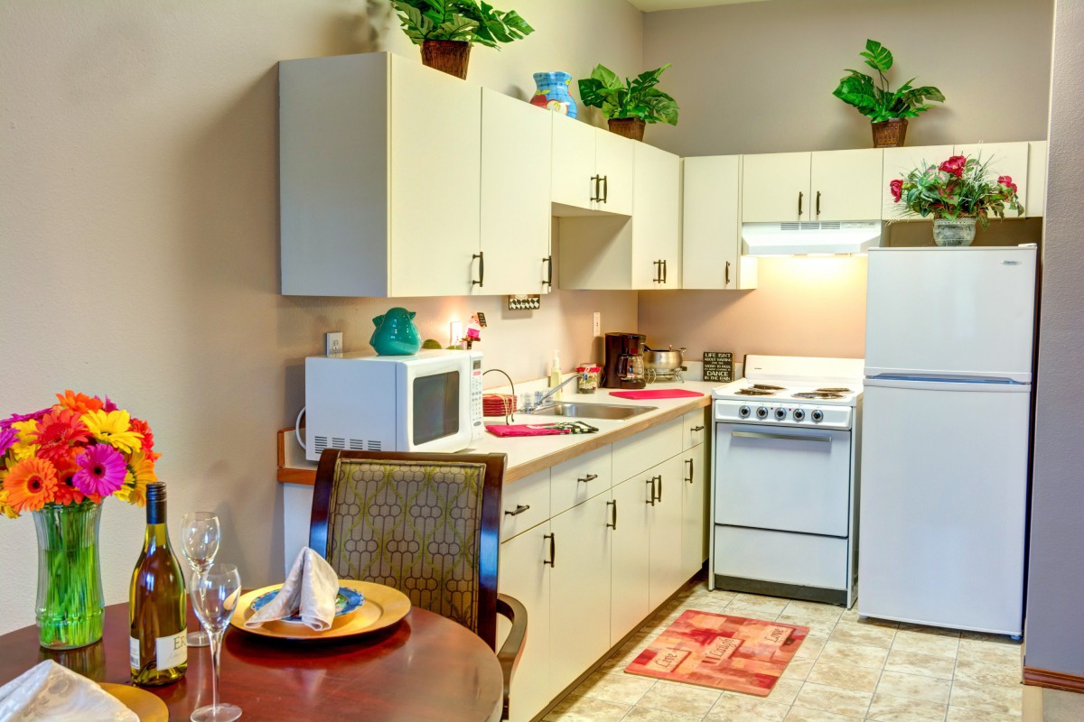 A compact apartment kitchen with a microwave, stove, refrigerator, and decorative plants.