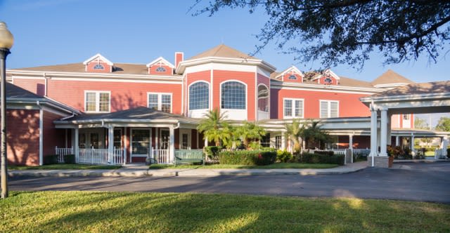 A large, elegant red building with a porch and surrounding greenery.