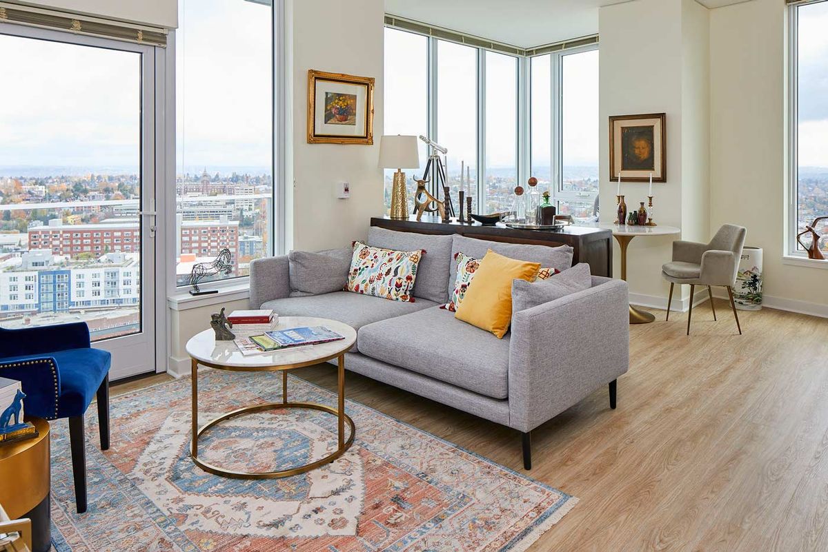 A modern living room with a gray sofa, coffee table, and large windows offering a city view.
