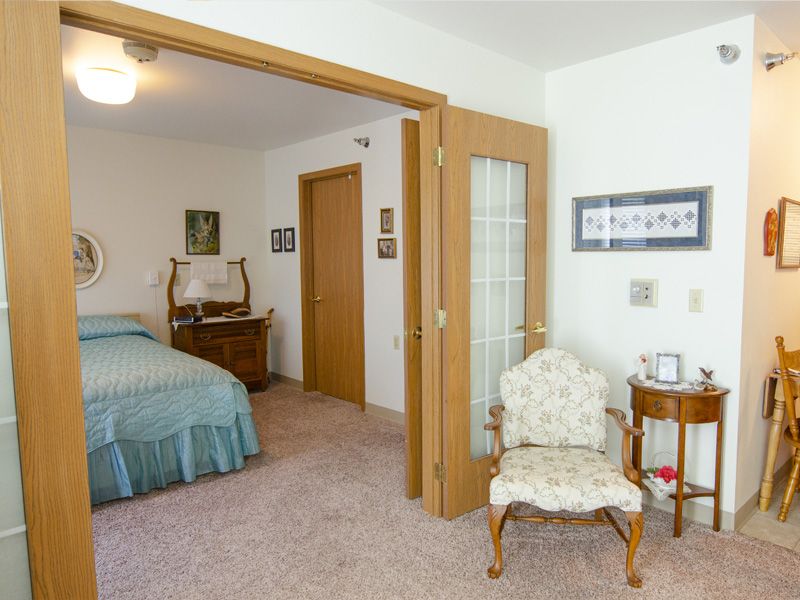 A cozy bedroom with vintage furniture and decor, featuring a bed, an upholstered chair, and a wooden dresser.