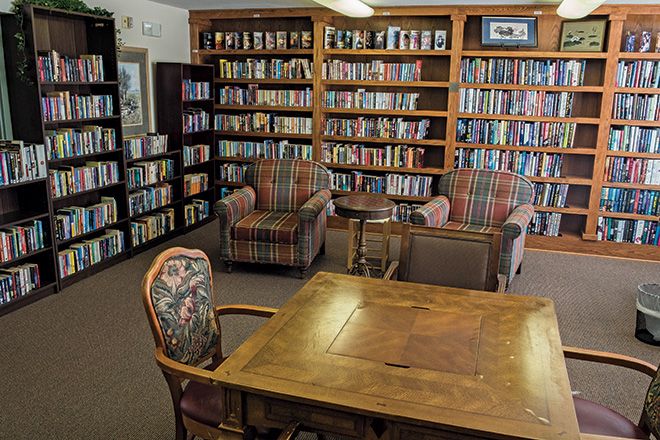 A cozy library corner with bookshelves, comfortable chairs, and a wooden table.