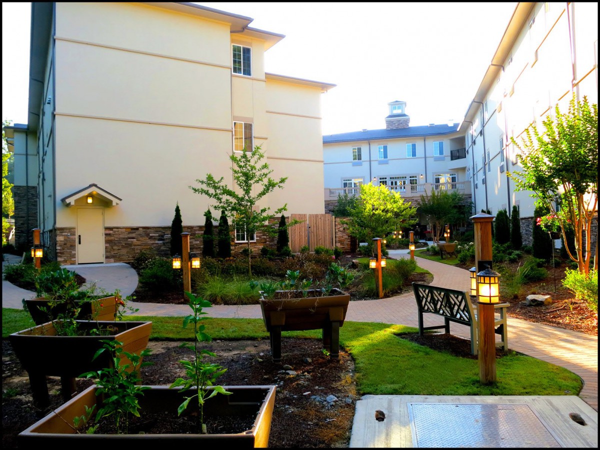 A beautifully landscaped garden area between buildings with benches and a pathway.