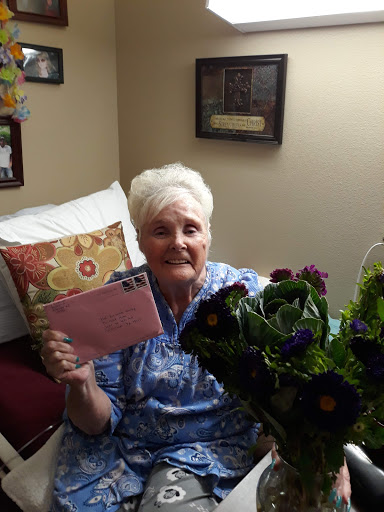 A joyful elderly woman holding a card and surrounded by beautiful flowers.