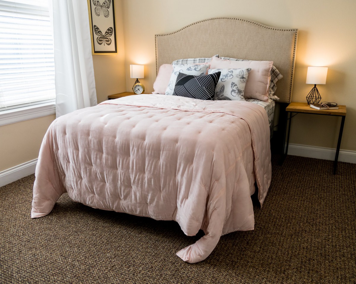 A cozy bedroom with a neatly made bed, side lamps, and neutral decor.