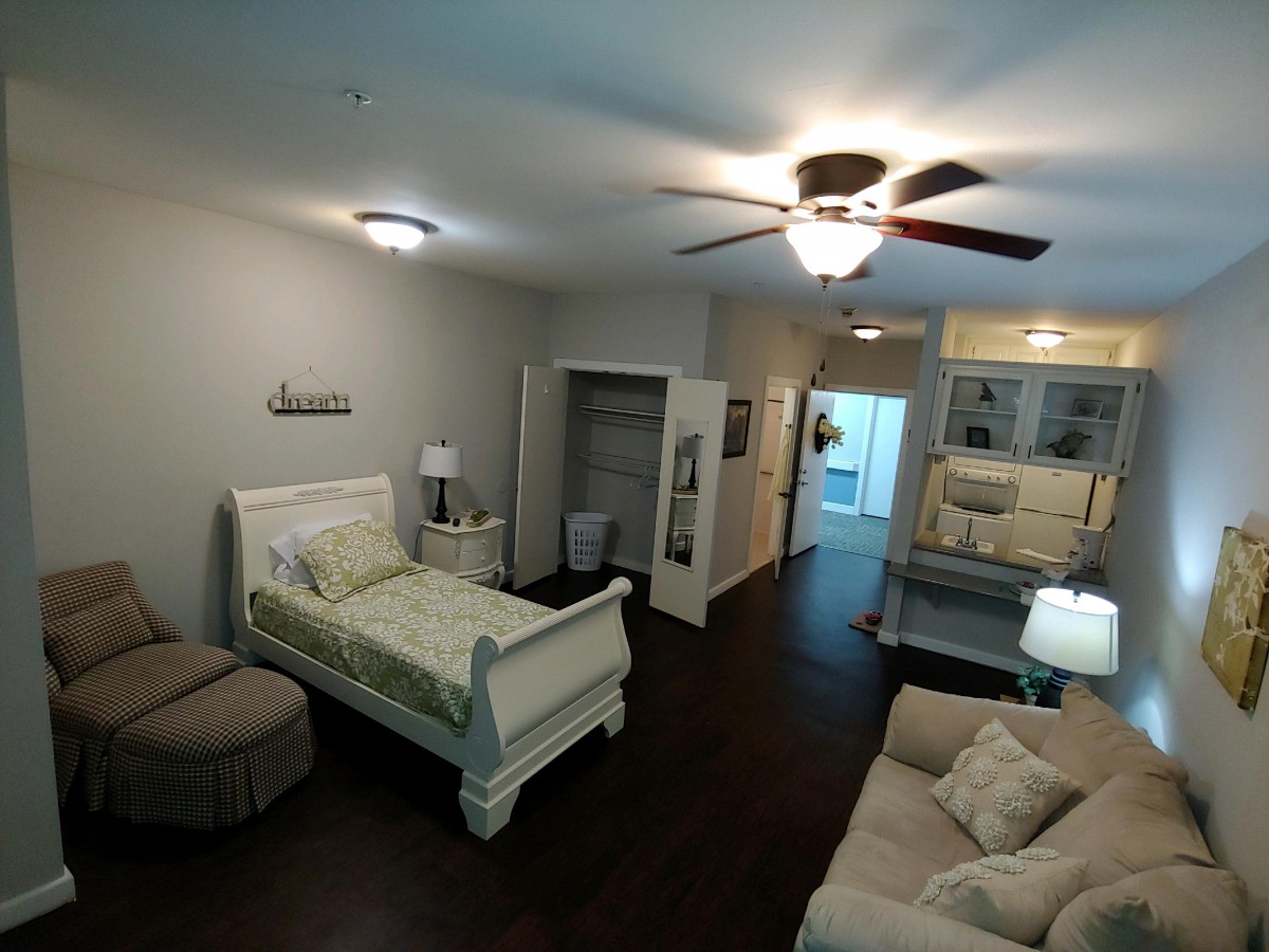 A cozy bedroom featuring a bed, sofa, and ceiling fan with wooden flooring.