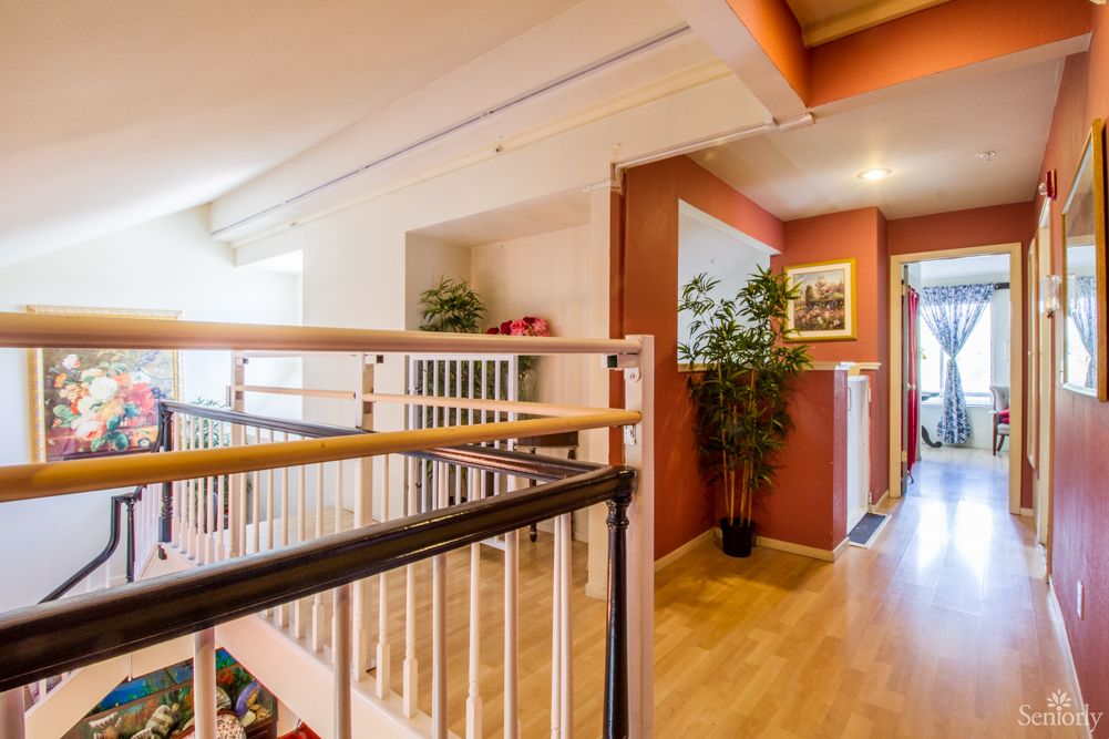 A well-lit hallway with wooden flooring, featuring a staircase and decorative plants.