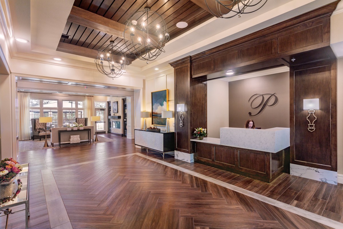 A luxurious hotel lobby with wooden flooring, elegant chandeliers, and a modern reception desk.