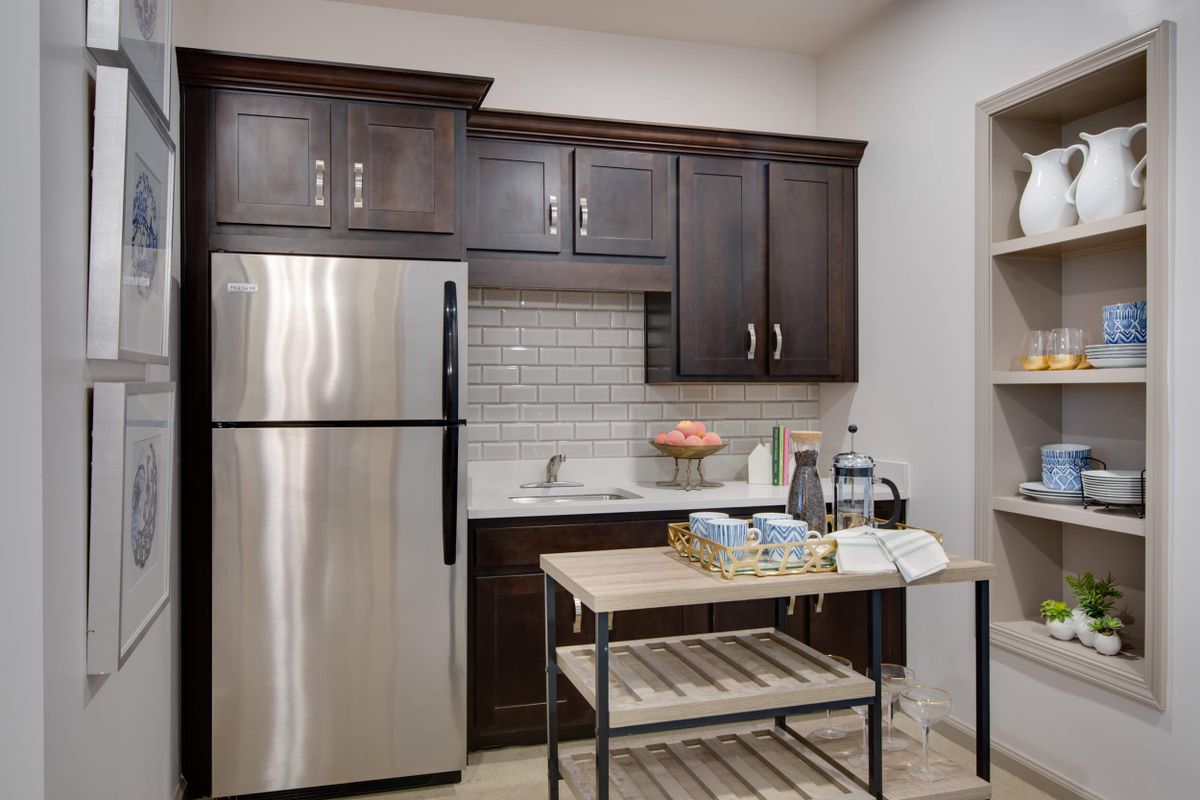 A modern kitchen with dark cabinets, a stainless steel fridge, and a small island cart.