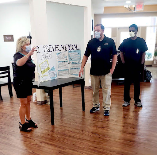 A group of individuals engaged in a presentation, discussing information displayed on a sign at a table.