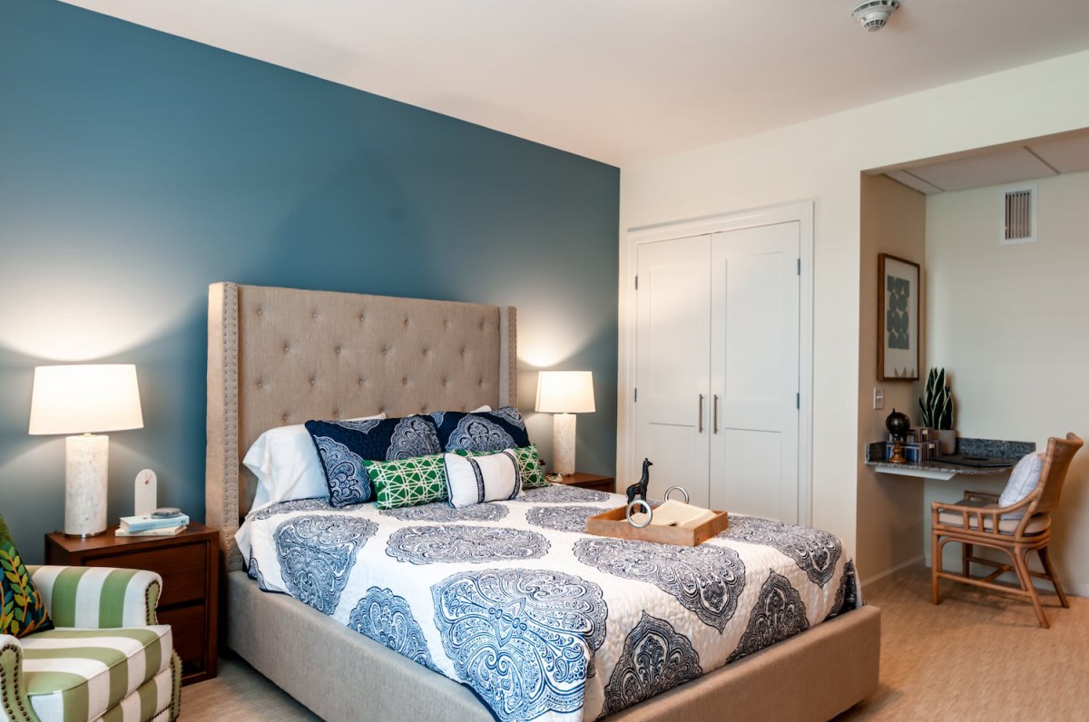 A modern bedroom with a blue accent wall, featuring a stylish bed with decorative pillows and a nightstand lamp.
