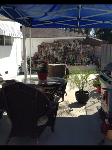 A cozy backyard patio with chairs and potted plants under a shade.