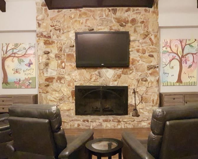 A cozy living room features a stone fireplace with a mounted television above, flanked by two comfortable armchairs.