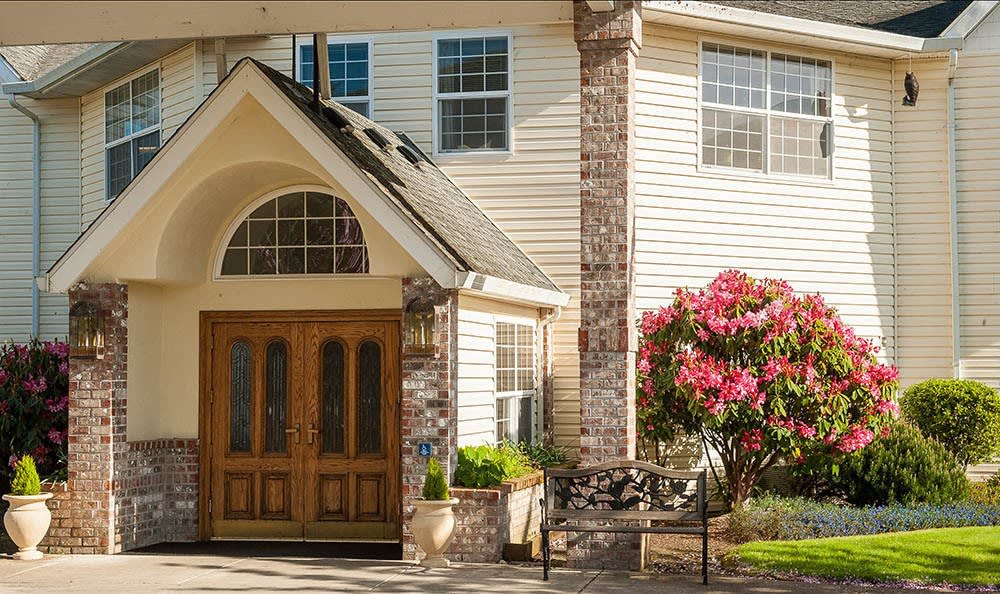 A welcoming house entrance with wooden doors and blooming flowers.