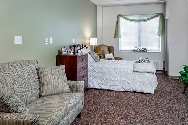 A cozy bedroom featuring a bed, armchair, and dresser with soft lighting.