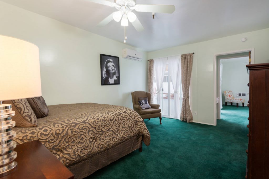 A cozy bedroom featuring a green carpet, decorated with a bed, chair, and wall art.