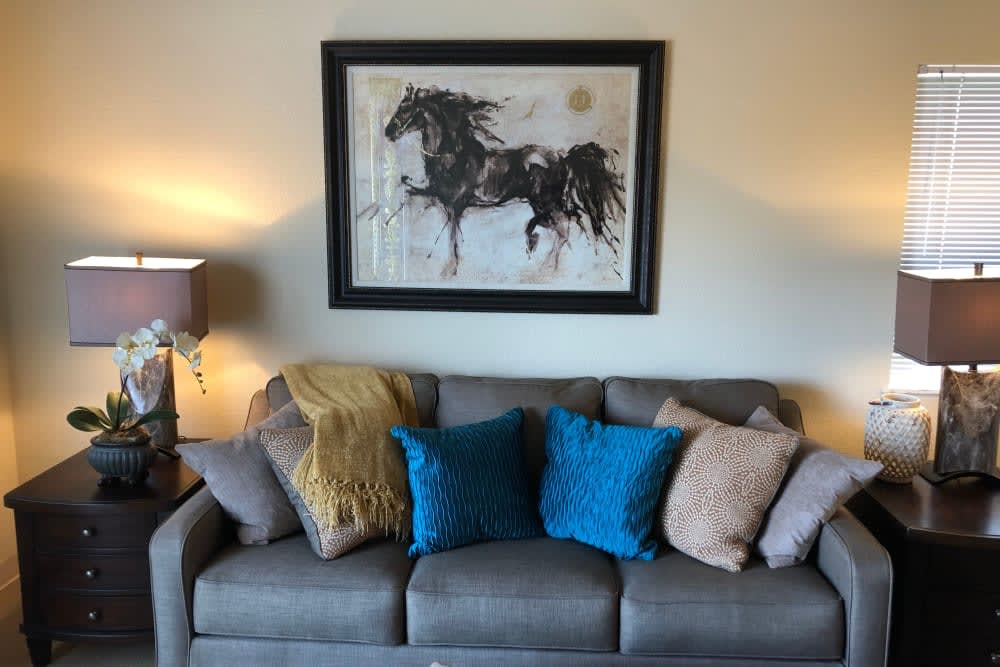 A cozy living room with a gray sofa adorned with colorful pillows, featuring a striking horse painting on the wall.