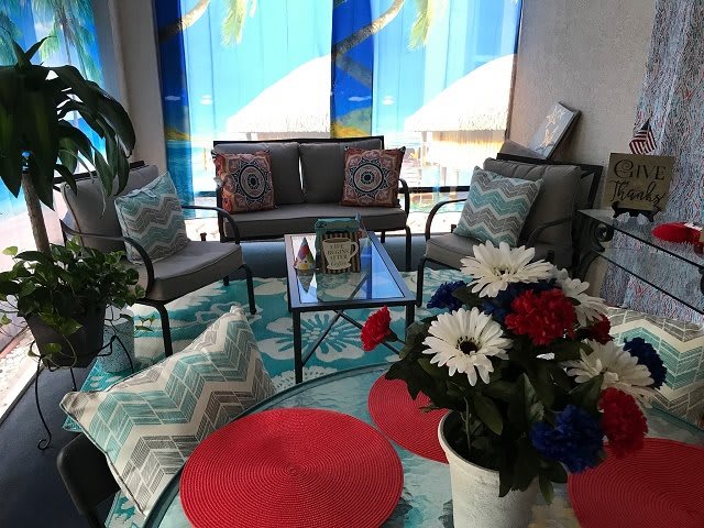 A cozy living room setup featuring cushioned seating, a rug, decorative pillows, and a floral arrangement.