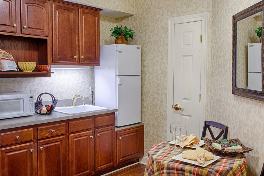 A cozy kitchen with wooden cabinets, a white refrigerator, and a small dining table covered with a plaid tablecloth.