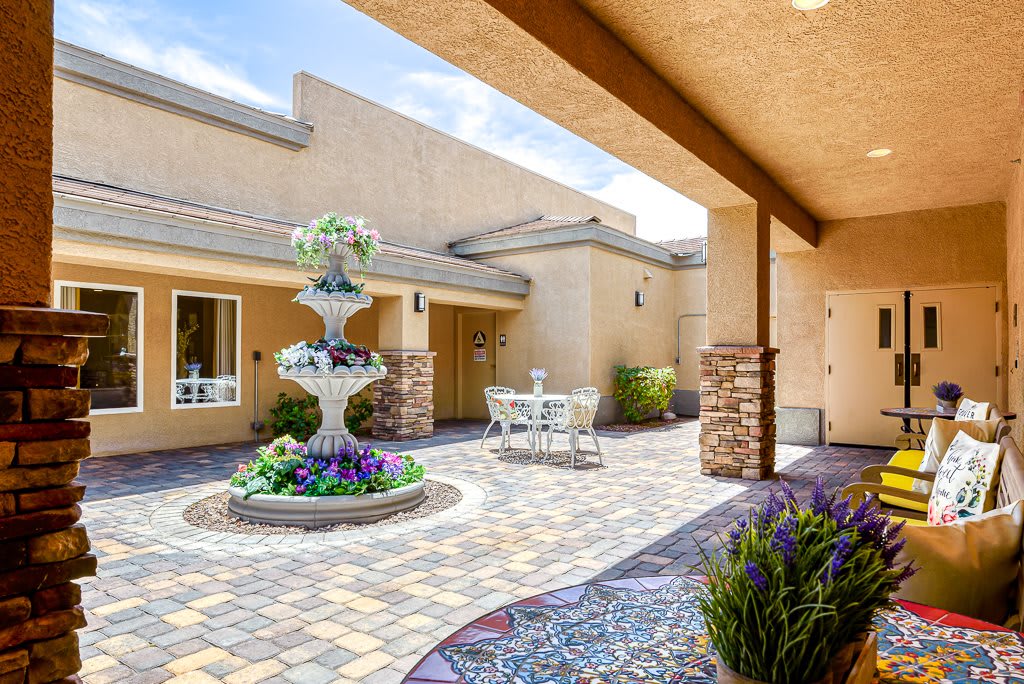 A tranquil courtyard featuring a decorative fountain and patio seating, surrounded by neatly arranged pavers and colorful landscaping.