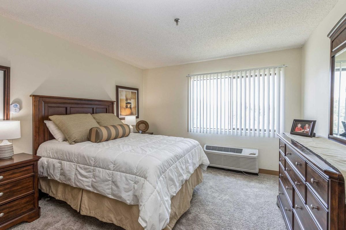 A cozy bedroom with a neatly made bed, soft lighting, and ample natural light coming through the window.