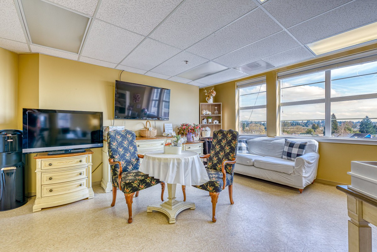 A cozy living room featuring a dining table with patterned chairs, sofas, and wall-mounted televisions.