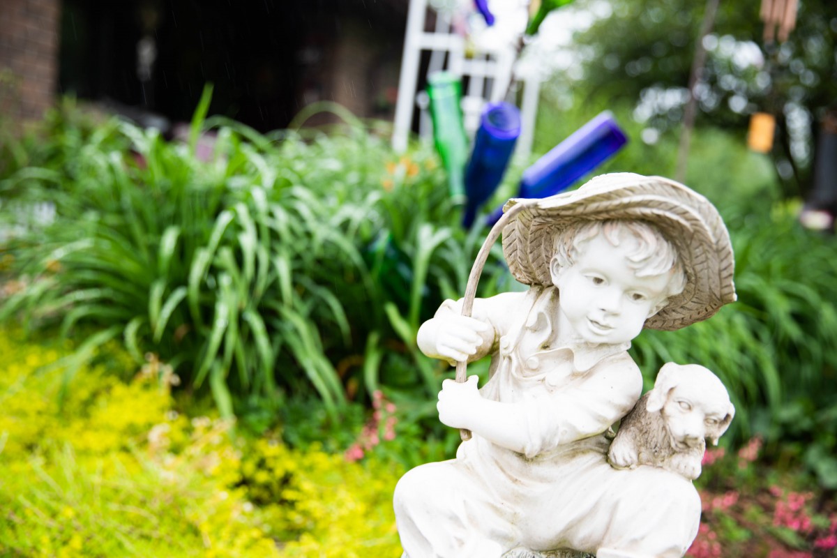 A garden sculpture of a child holding a fishing pole amidst lush greenery.