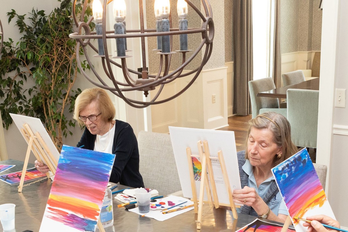 Two elderly women enjoying a painting session indoors.