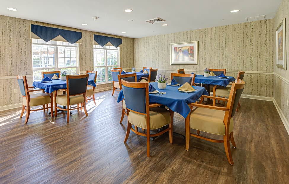 A dining room with tables and chairs set up, featuring blue tablecloths and wooden furniture.