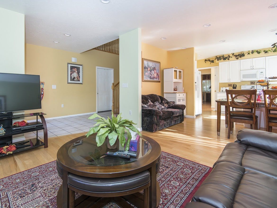 A cozy living room with a sofa, wooden tables, a rug, and decorative plants.