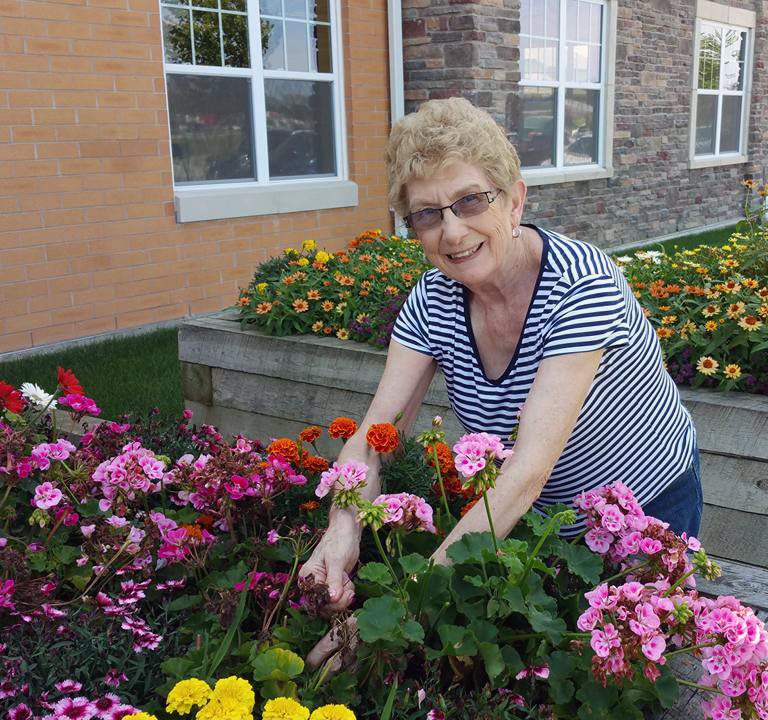 A woman tending to her flower garden outside a building.