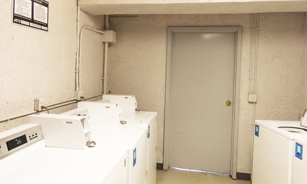 A small laundry room with multiple washing machines lined up against the wall.