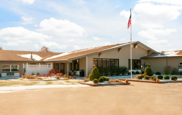 A single-story building with an American flag flying in front, surrounded by landscaped grounds and a parking area.
